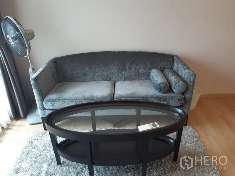 Condominium for rent or sale in Watthana, Bangkok - Gray velvet sofa with an oval glass coffee table set on a rug.