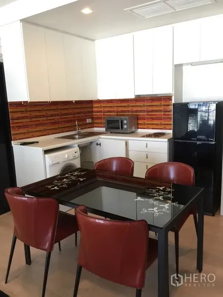 公寓 出租在Watthana, Bangkok - 现代开放式厨房，白色橱柜、橙色防溅墙、玻璃餐桌，配洗衣机与黑色冰箱的通罗公寓。