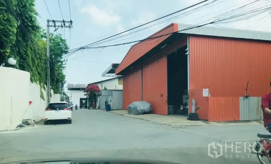 货栈 出租在Bueng Kum, Bangkok - 街景：橙色金属外墙的仓库，入口宽敞，位于曼谷汶甘区的工业小巷。