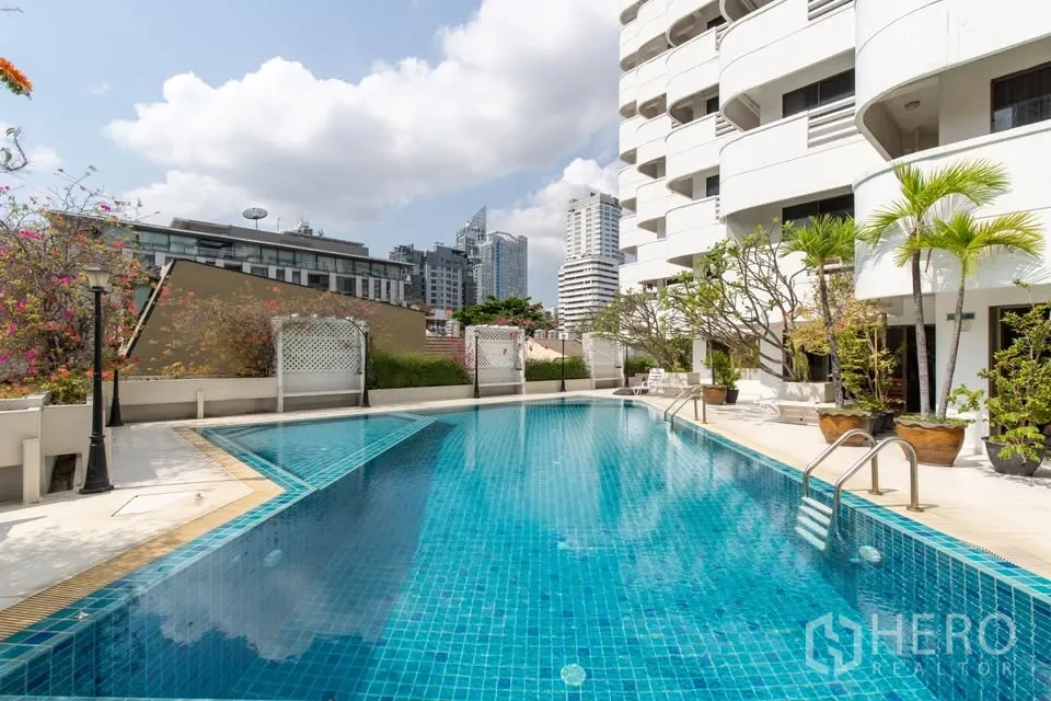 คอนโด for rent in Watthana, Bangkok - สระว่ายน้ำกลางแจ้งข้างอาคารคอนโดสีขาว มองเห็นวิวสกายไลน์เมือง.