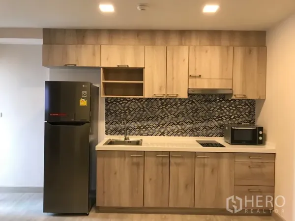 公寓 出租在Watthana, Bangkok - 一体化厨房，木质橱柜、马赛克防溅板、灶台、水槽、微波炉与冰箱。