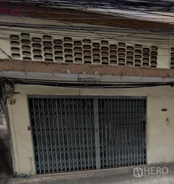 店屋 出租在Khlong Toei, Bangkok - 空堤区街边店屋外观，金属折叠闸门、通风砌块与人行道，上方布满电缆。