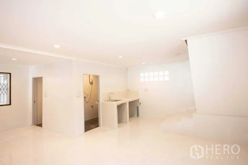 Home Office for rent in Watthana, Bangkok - Open-plan ground floor with pantry sink, bathroom access, and stairs in a clean white interior.