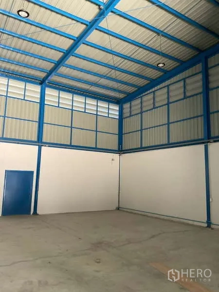 Warehouse for rent in Bang Bua Thong, Nonthaburi - Spacious interior corner showing a blue-framed door, concrete floor and high roof.