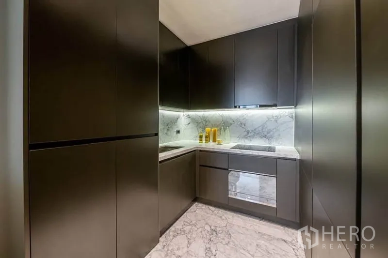 คอนโด ให้เช่าหรือขายในWatthana, Bangkok - ครัวรูปตัวแอล ตู้สีเข้ม เคาน์เตอร์และผนังหินอ่อน ไฟใต้ตู้ พร้อมเตาและเตาอบบิลท์อิน