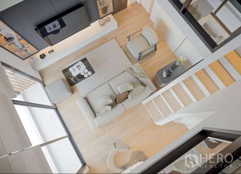 Condominium for rent in Huai Khwang, Bangkok - Top-down view of living area with sofa, rug and stairway from the mezzanine.