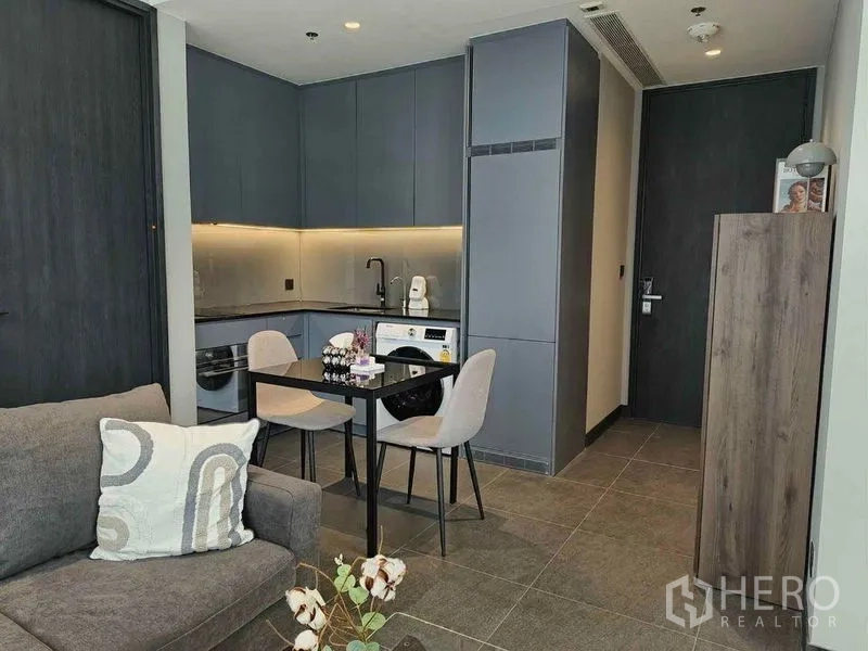 Condominium for rent in Bang Rak, Bangkok - Compact kitchen with built-in cabinets, two-seat dining set, and in-unit washing machine.