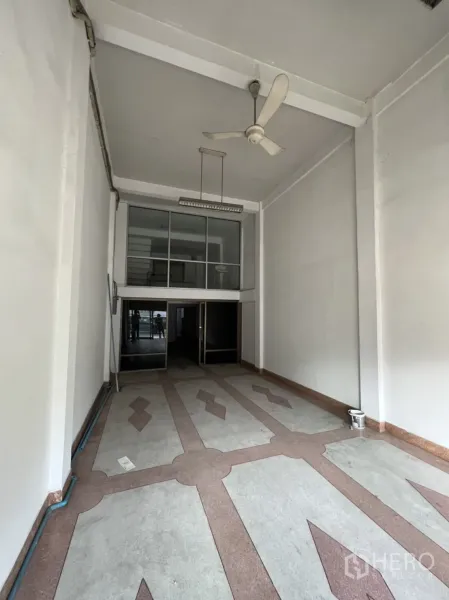 店屋 出租在Phra Khanong, Bangkok - 纵深开间零售区域，白色高墙与吊灯，装饰地砖通向玻璃门。