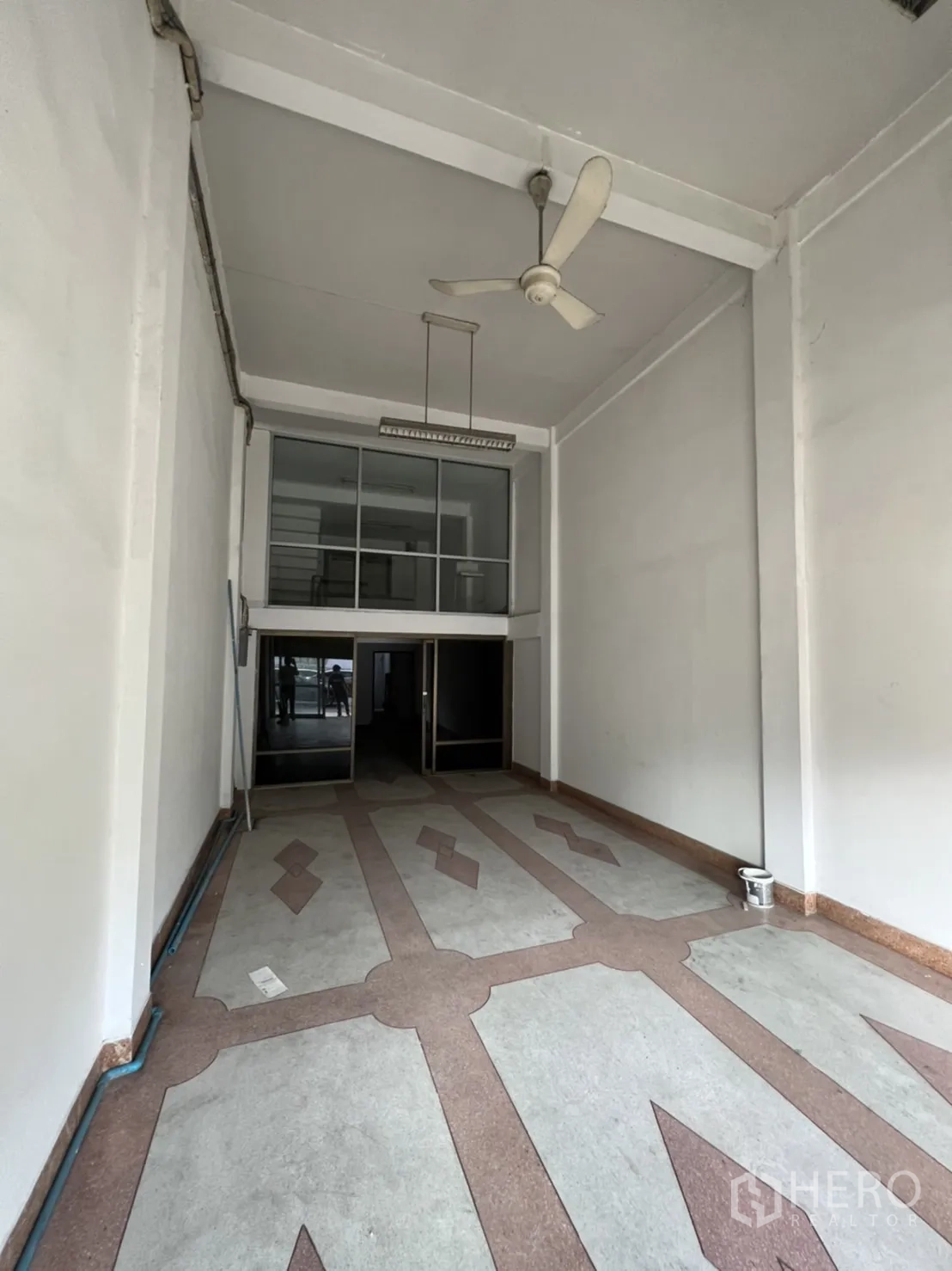 店屋 出租在Phra Khanong, Bangkok - 纵深开间零售区域，白色高墙与吊灯，装饰地砖通向玻璃门。