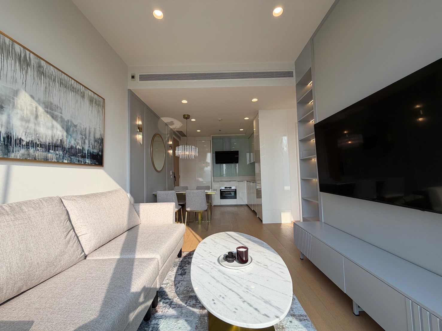 公寓 出租在Bang Rak, Bangkok - 采光充足的客厅，设大屏电视墙、内置置物架、大理石茶几与开放式厨房。