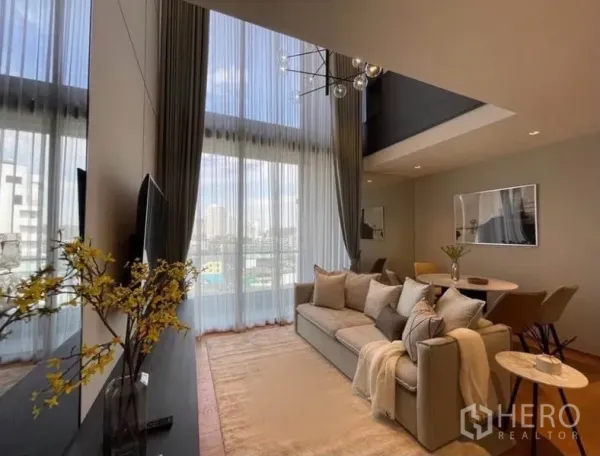 คอนโด ให้เช่าในKhlong Toei, Bangkok - ห้องนั่งเล่นสว่าง โซฟาโทนกลาง พรมผืนใหญ่ และโต๊ะทานอาหารทรงกลมใต้ผนังกระจกสองชั้น