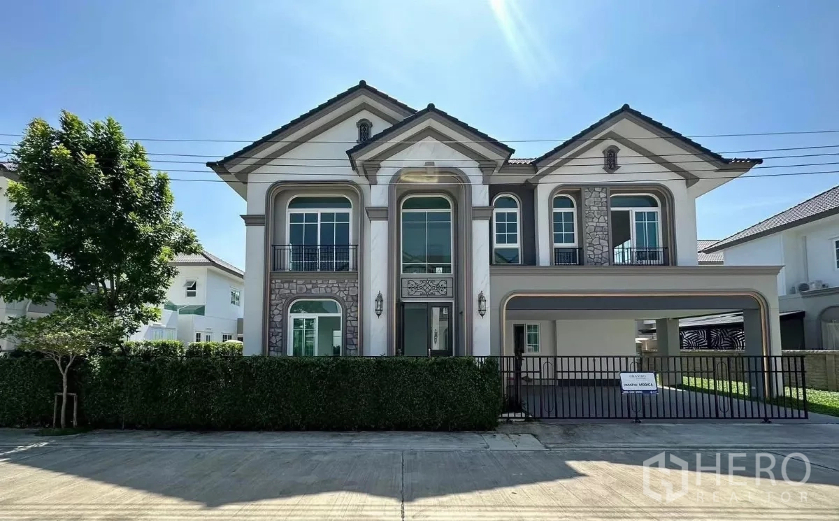 Detached House for rent in Bang Phli, Samut Prakan - Elegant two-story detached house with stone accents, balconies, and a gated carport under clear sky.
