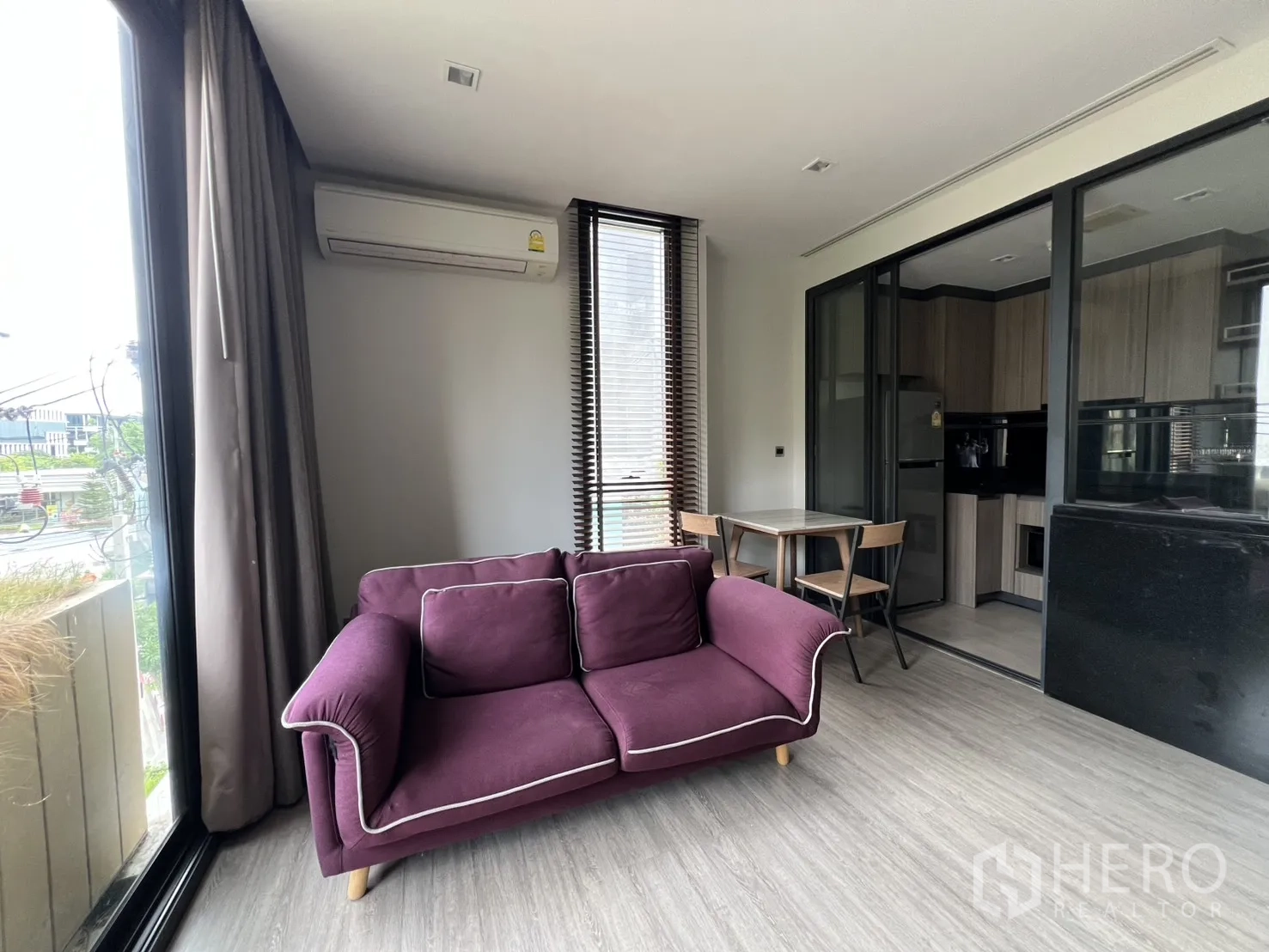 Condominium for rent in Watthana, Bangkok - Living area with a purple sofa facing large windows beside a glass-walled kitchen.