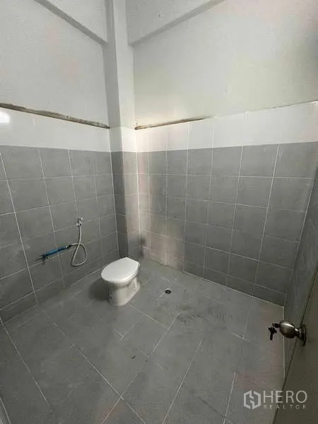 คลังสินค้า ให้เช่าในSamut Sakhon - ห้องน้ำปูกระเบื้องสีเทา มีโถสุขภัณฑ์และสายชำระในโกดัง