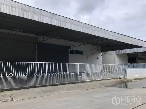 Warehouse for rent in Bang Bo, Samut Prakan - Gated entrance with sliding metal fence and covered bays with roller shutters.