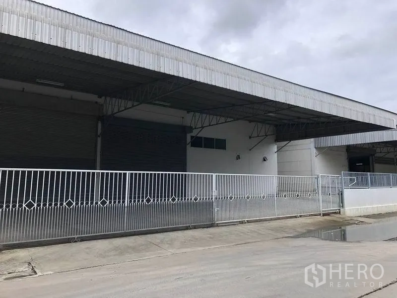 Warehouse for rent in Bang Bo, Samut Prakan - Gated entrance with sliding metal fence and covered bays with roller shutters.
