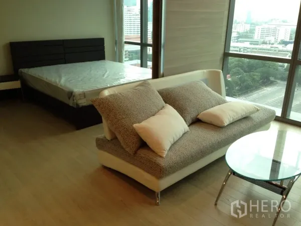 Condominium for rent in Watthana, Bangkok - Open plan lounge beside a bed near large corner windows with Bangkok city outlook.
