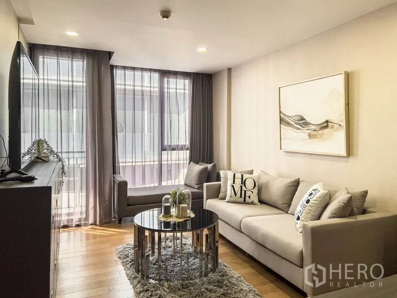 Condominium for rent in Pathum Wan, Bangkok - Living area with large windows, sofa set, and round coffee table on a plush rug.