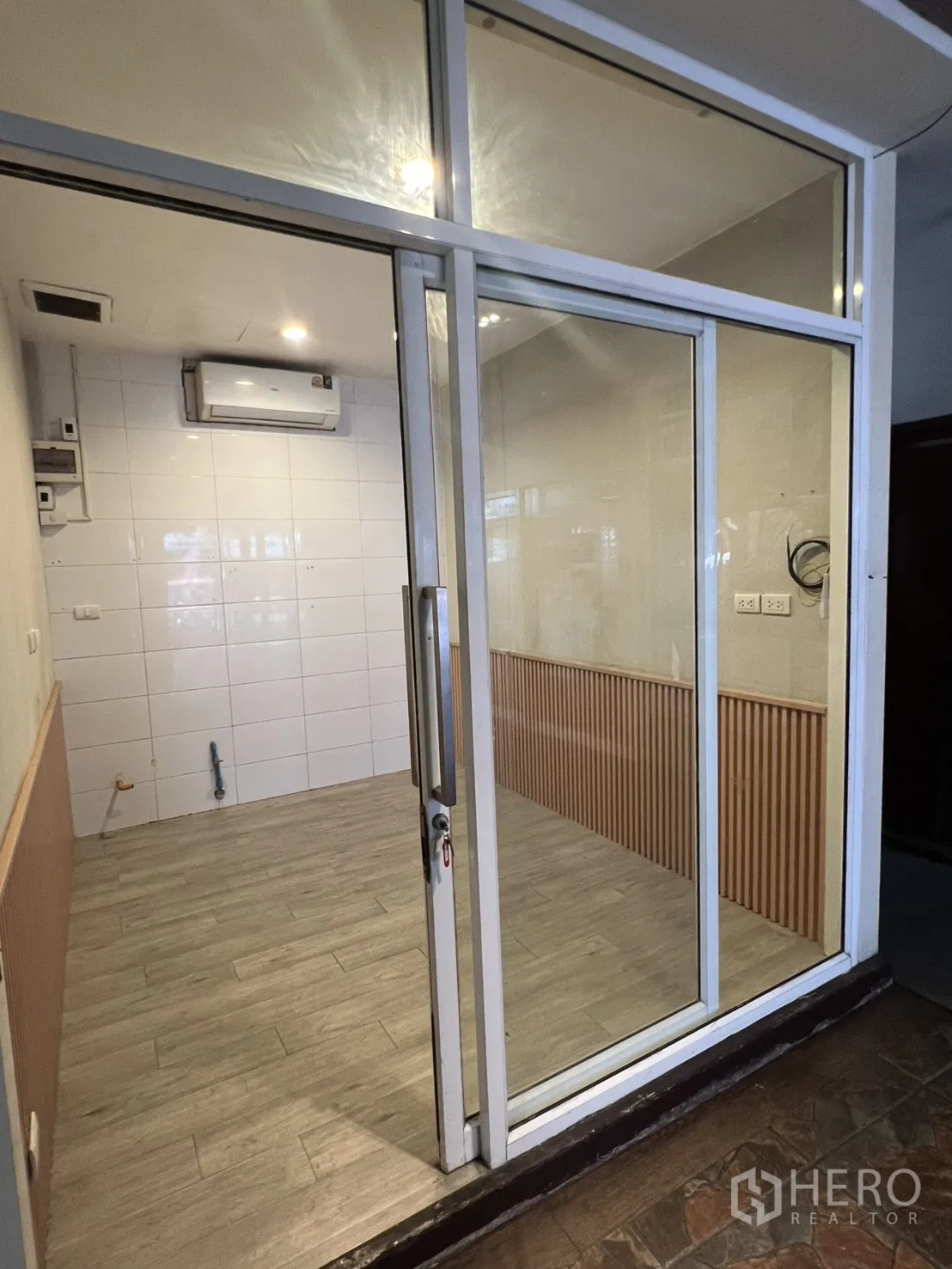 零售空间 出租在Watthana, Bangkok - 素坤逸8㎡零售小铺，整面玻璃推拉门、木纹地砖、白色瓷砖墙与挂壁空调。