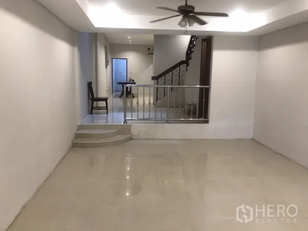 Home Office for rent in Khlong Toei, Bangkok - Spacious ground-floor living area with glossy tile floors, ceiling fan, and split-level steps with a metal railing.