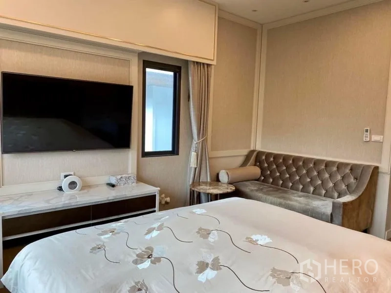 Detached House for rent or sale in Prawet, Bangkok - Bright bedroom with wall-mounted TV and tufted sofa by the window.