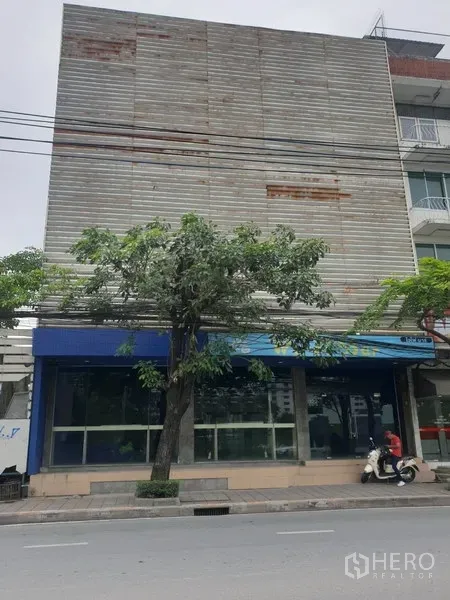พื้นที่ขายปลีก ให้เช่าในWatthana, Bangkok - อาคารค้าปลีกติดถนน หน้าร้านกระจกเต็มแนว มีกันสีน้ำเงินและต้นไม้ริมทางเท้า