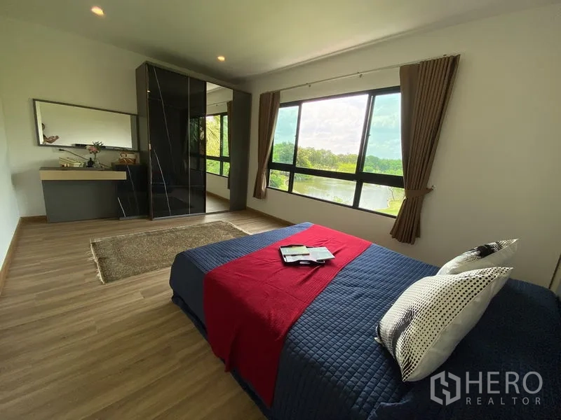 Townhouse for rent in Bang Kapi, Bangkok - Large bedroom with panoramic windows facing lakeside greenery and fitted wardrobe.