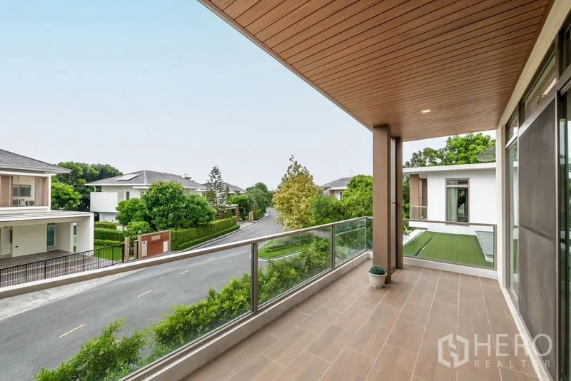 บ้าน ขาย - ระเบียงกว้างพร้อมราวกระจก มองเห็นถนนในหมู่บ้านที่ร่มรื่น