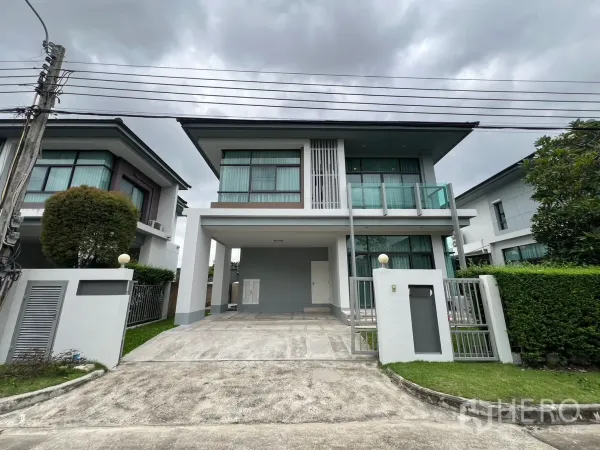 Detached House for rent in Bang Kapi, Bangkok - Modern two-storey detached house with glass balcony, gated driveway and hedges under a cloudy sky in Bang Kapi.