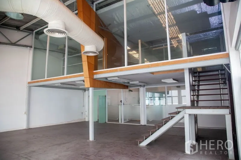 货栈 出租在Prawet, Bangkok - 夹层办公室玻璃围合，外露风管与楼梯通达的工业仓库内景。
