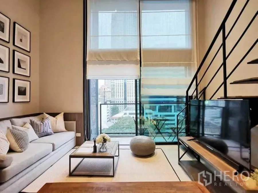 公寓 出租在Bang Rak, Bangkok - 客厅面向阳台与高窗，远眺城市天际线与夹层楼梯。