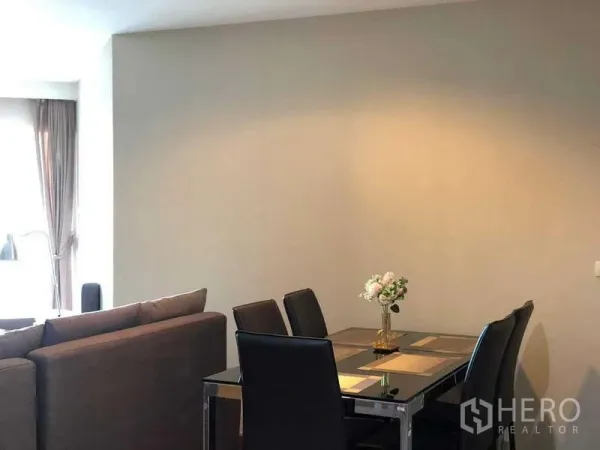 Condominium for sale in Huai Khwang, Bangkok - Dining area with glass-top table and four leather chairs beside the living room.