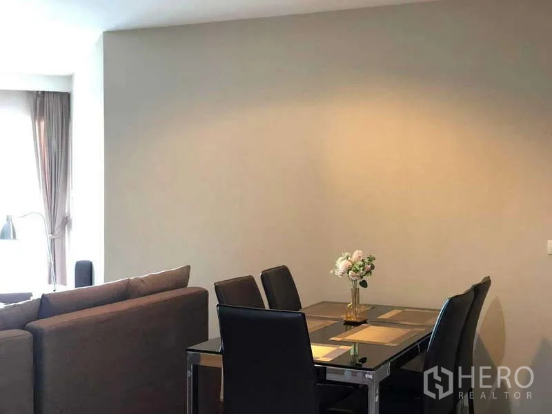 Condominium for sale in Huai Khwang, Bangkok - Dining area with glass-top table and four leather chairs beside the living room.