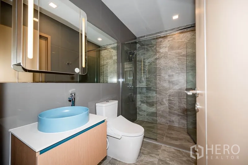 คอนโด ให้เช่าในWatthana, Bangkok - ห้องน้ำสมัยใหม่ อ่างล้างมือสีฟ้า ห้องอาบน้ำกระจก และกระเบื้องหินสีเทา
