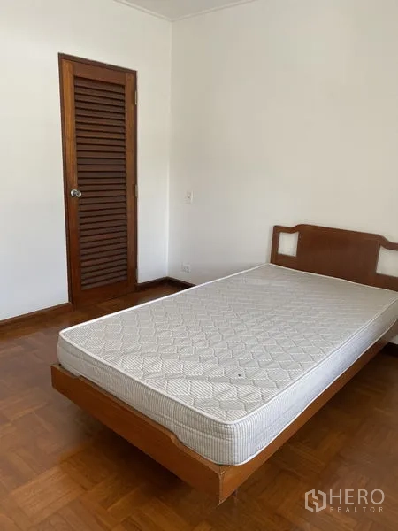 Apartment for rent in Khlong Toei, Bangkok - Second bedroom from another angle with louvered closet door and wooden bed.