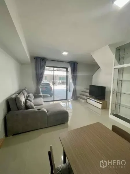 Townhouse for rent in Bang Phli, Samut Prakan - Open-plan living area with sliding glass doors to the carport, TV stand and staircase.