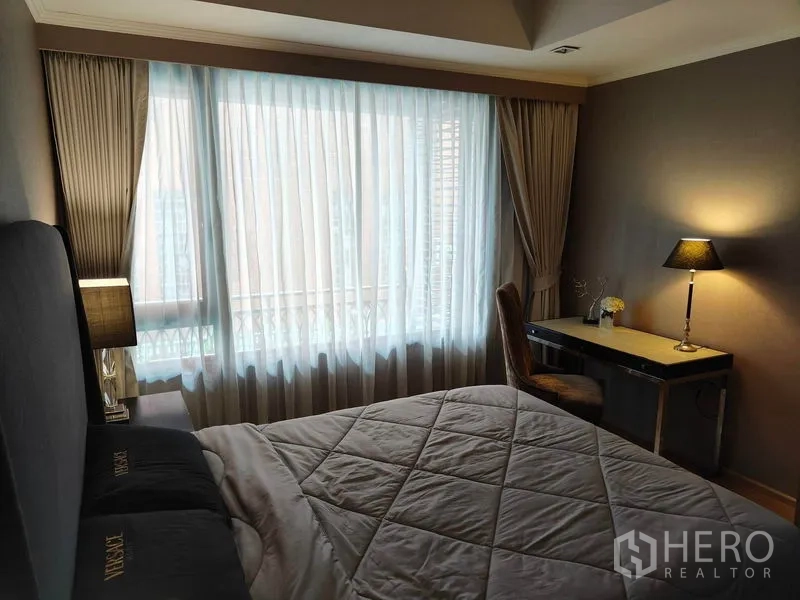 Condominium for rent or sale in Pathum Wan, Bangkok - Bedroom with study desk by the window, quilted bedding, and soft ambient lighting.