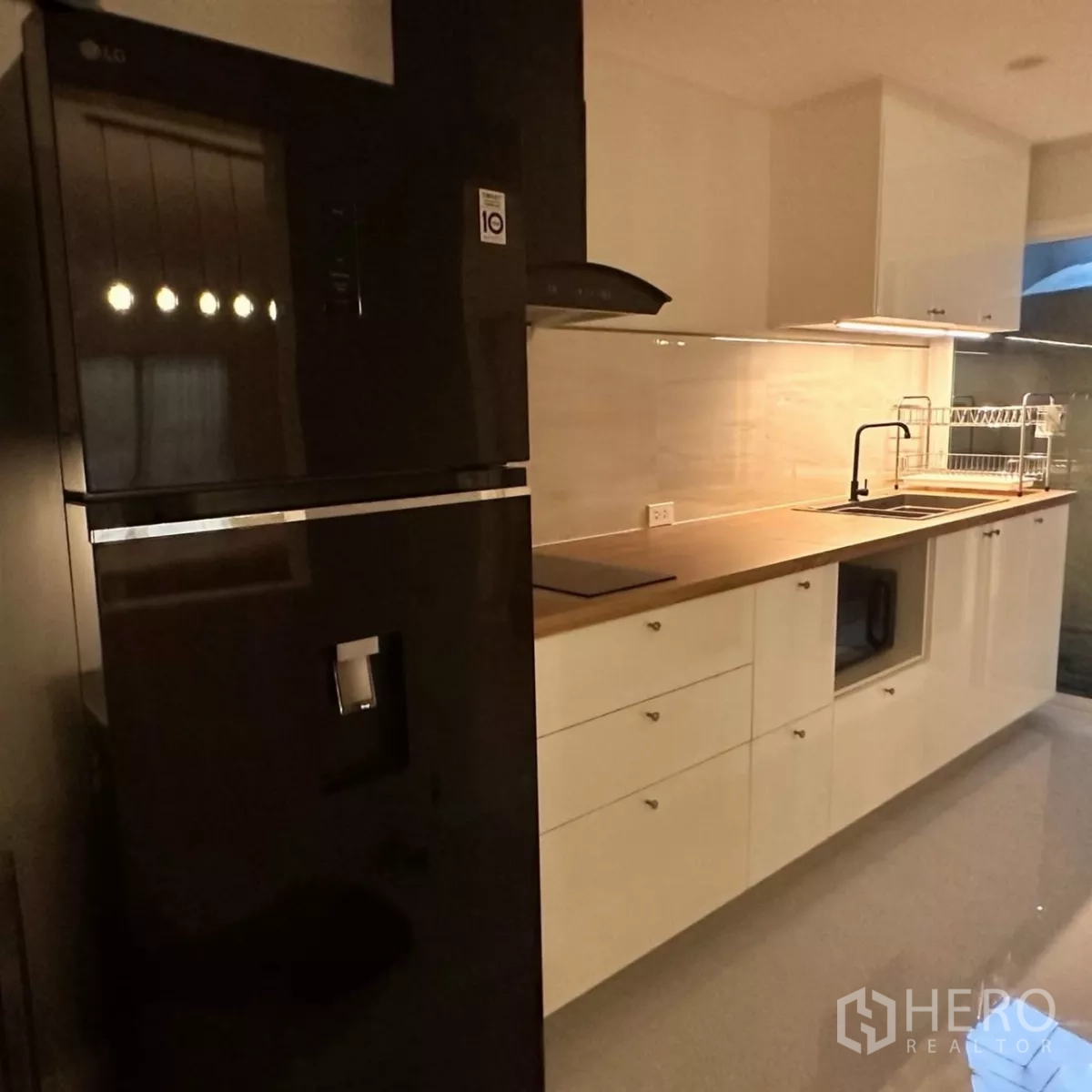 Townhouse for rent in Bang Phli, Samut Prakan - Evening dining and kitchen view with pendant lights, table set and built-in cabinets.