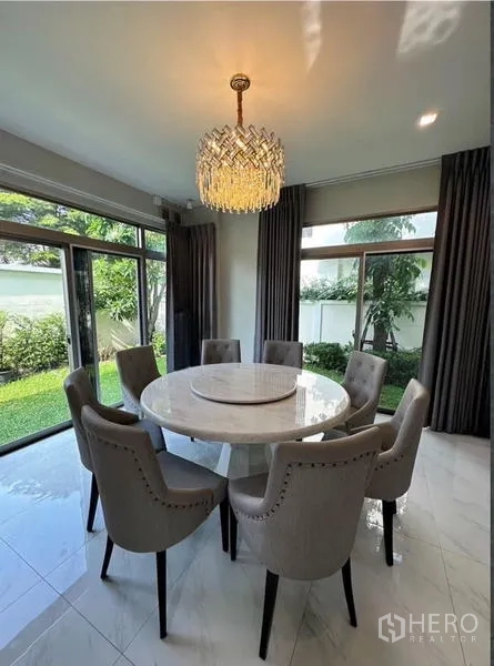 Detached House for rent in Bang Phli, Samut Prakan - Bright dining room with a round marble table, eight upholstered chairs and a chandelier facing the garden.