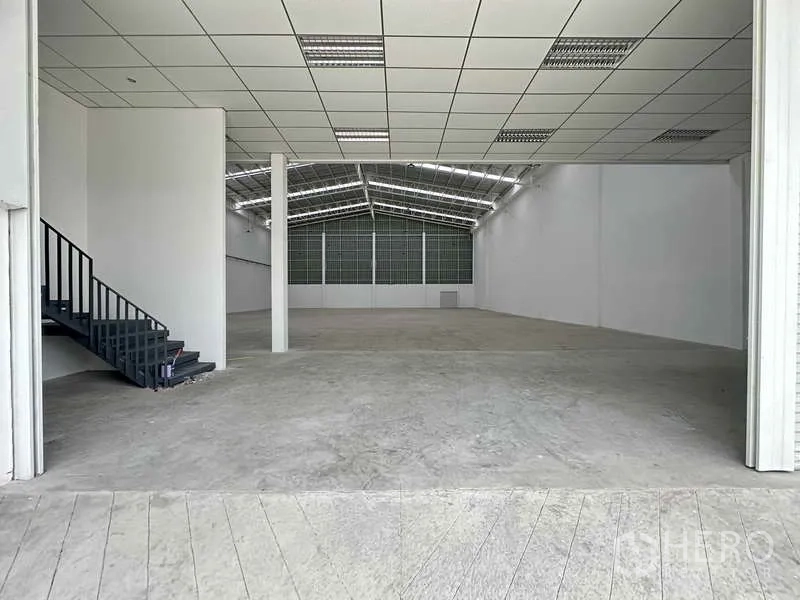 工厂 出租在Khlong Luang, Pathum Thani - 高挑仓库内部，混凝土地面，侧边楼梯通往夹层办公室。