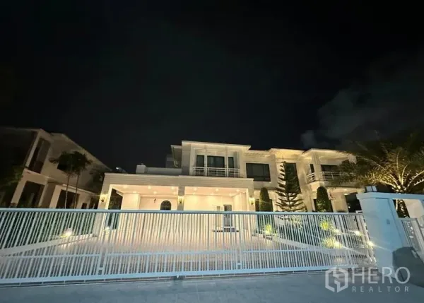 Detached House for rent in Bang Phli, Samut Prakan - Night view of the illuminated modern house behind a white metal gate.