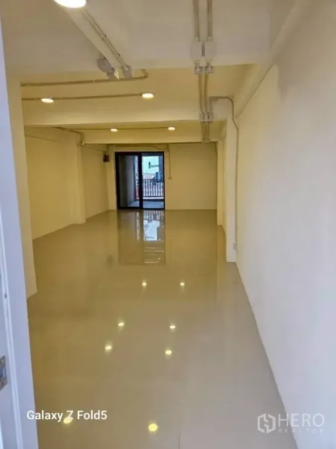 พื้นที่ขายปลีก ให้เช่า - พื้นที่ค้าปลีกโล่ง พื้นกระเบื้องเงา ไฟดาวน์ไลท์ ผนังสีขาว และประตูสู่ระเบียงด้านในสุด