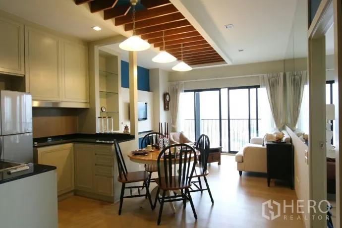 Condominium for rent or sale in Watthana, Bangkok - L-shaped kitchen with granite countertops, built-in storage and dining area under pendant lights.