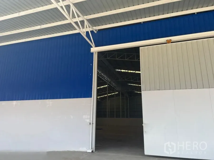 Warehouse for rent in Lat Krabang, Bangkok - Blue-and-white sliding steel warehouse door with covered entry.