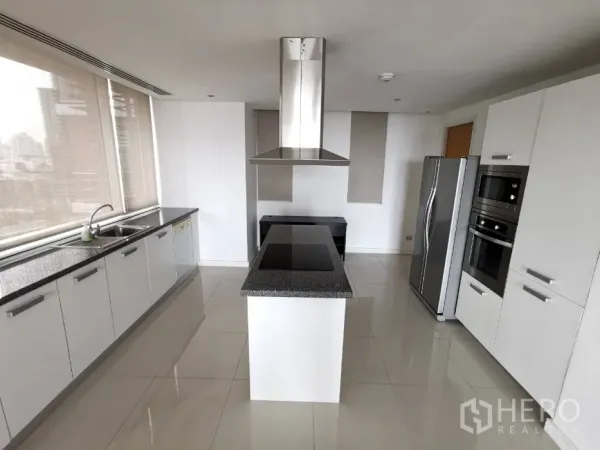 Condominium for rent in Watthana, Bangkok - Modern white kitchen with a granite island cooktop, stainless steel appliances, and wide windows with city views.