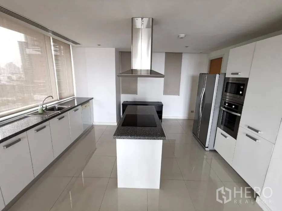 Condominium for rent in Watthana, Bangkok - Modern white kitchen with a granite island cooktop, stainless steel appliances, and wide windows with city views.