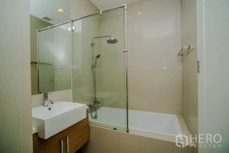 Condominium for rent or sale in Watthana, Bangkok - Modern bathroom with glass-enclosed shower over bathtub and vanity.