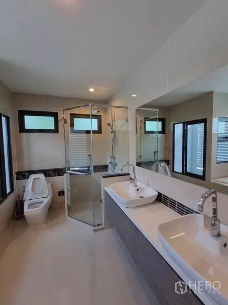 Detached House for sale in Suan Luang, Bangkok - Bright bathroom with double sinks, a glass shower enclosure and windows.