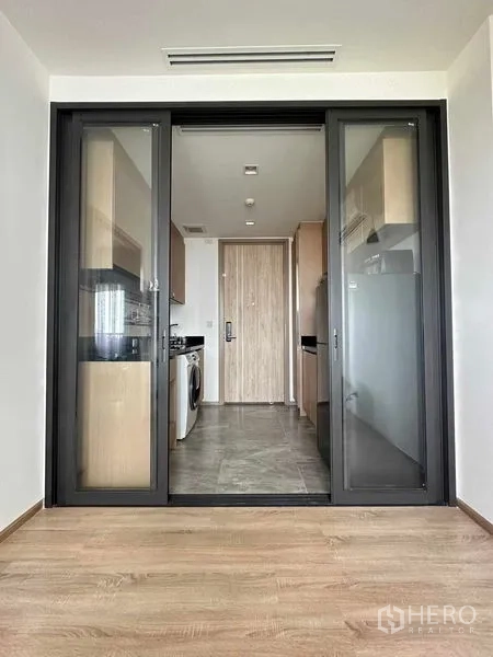 คอนโด ขายในWatthana, Bangkok - ห้องนั่งเล่นพื้นลามิเนต เชื่อมครัวปิดผ่านประตูบานเลื่อนกรอบอลูมิเนียมสีดำ