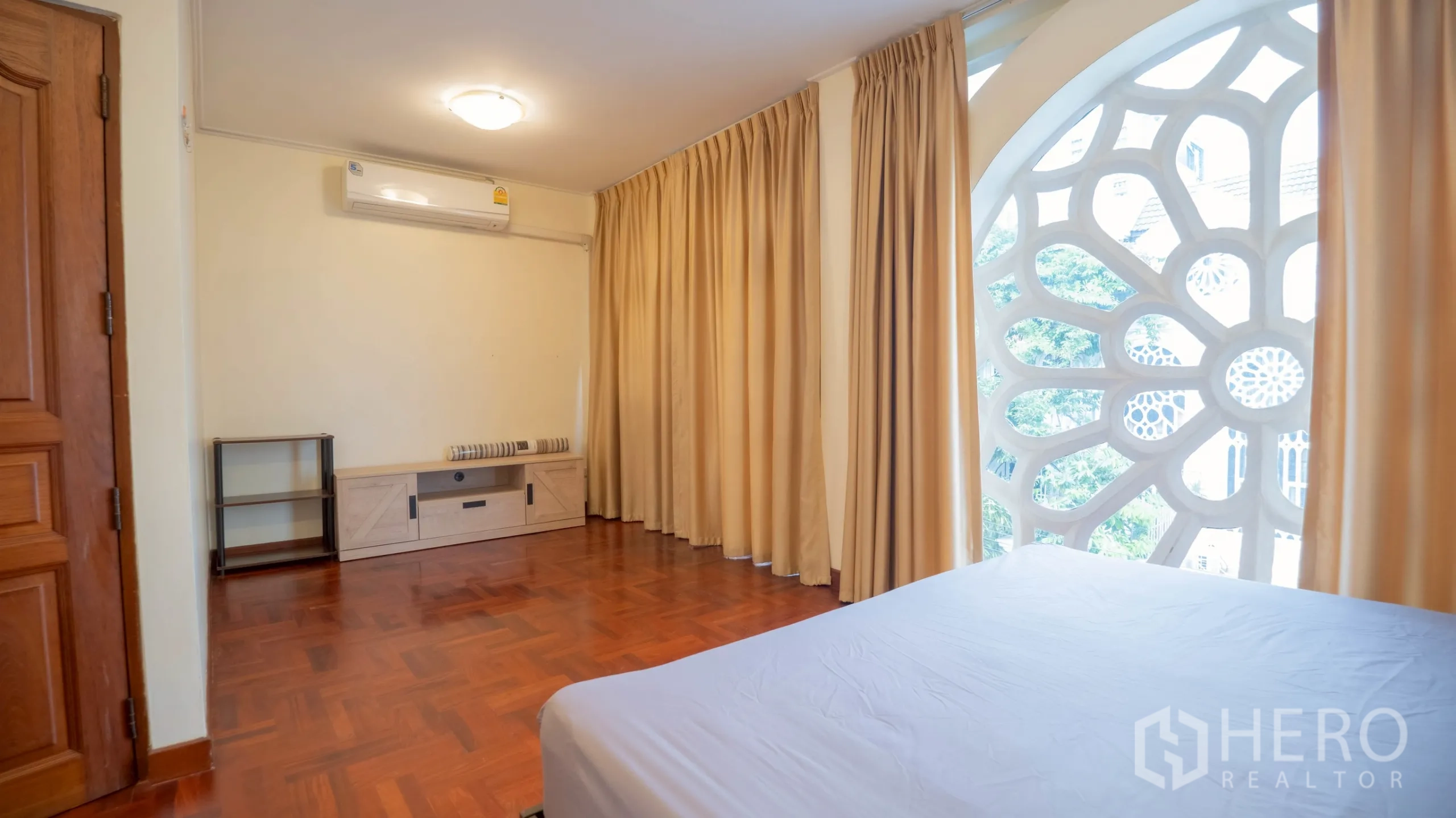 Townhouse for rent in Khlong Toei, Bangkok - Bedroom with rosette window, beige curtains, wood floor and TV console.